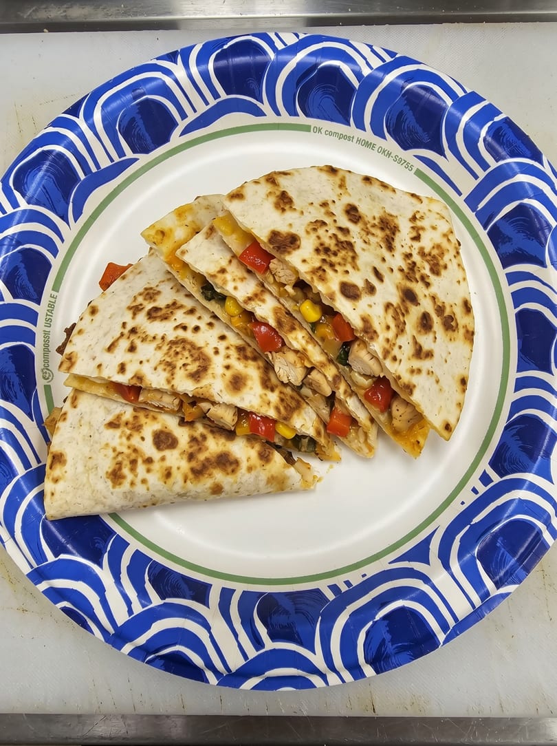 Chicken quesadillas with corn, red peppers, and black beans on a blue and white paper plate.
