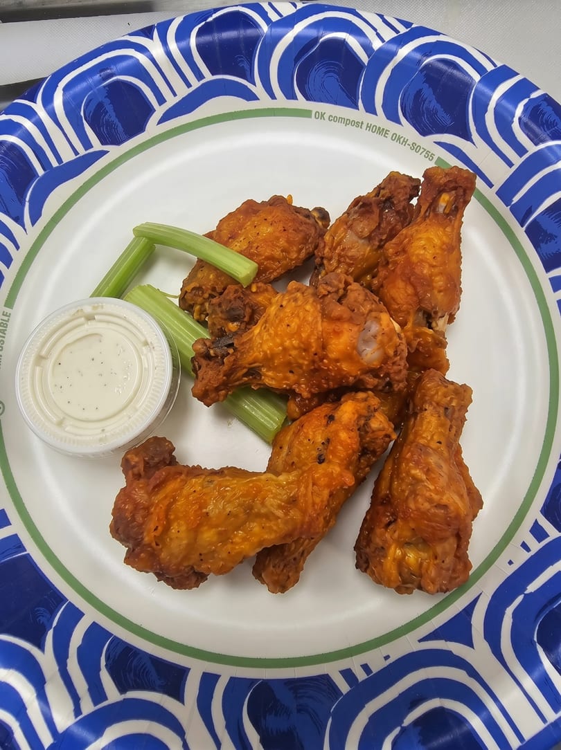Buffalo wings with celery sticks and a side of ranch dressing on a paper plate.