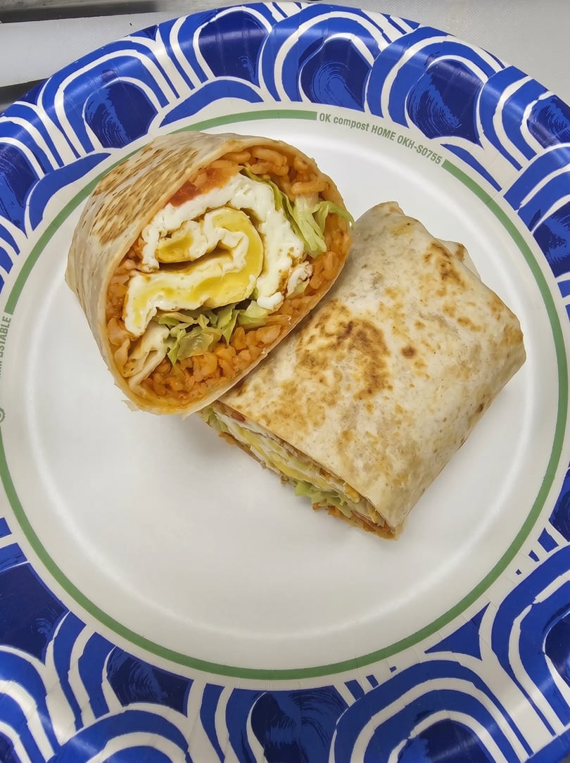 Two halves of a breakfast burrito with eggs, rice, and lettuce on a blue and white paper plate.