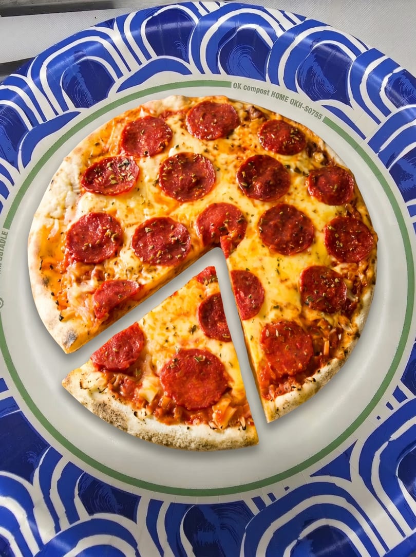 A pepperoni pizza with a slice removed, served on a blue and white patterned paper plate.